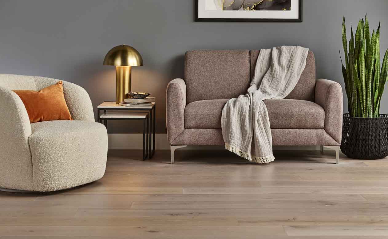 light hardwood flooring in living room with white boucle chair, beige couch and gold lamp